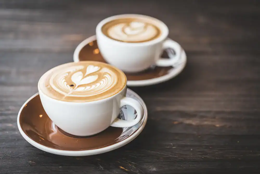 Two white cups of coffee with heart-shaped latte art sit on brown saucers atop a dark wooden table, capturing the cozy vibe of a cafe NYC afternoon.